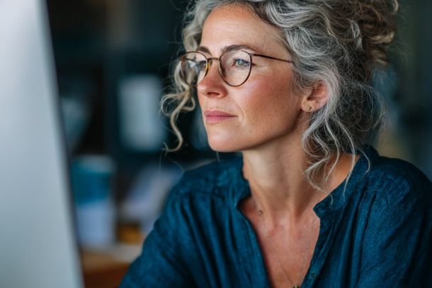 Eine Frau mittleren Alters schaut konzentriert in einen PC-Monitor